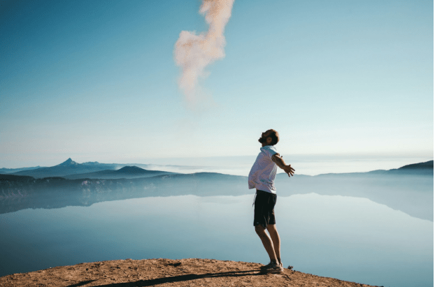 A man on mountain exhales smoke, symbolizing release of inner struggles. Success story at Men’s Mental Health Institute.