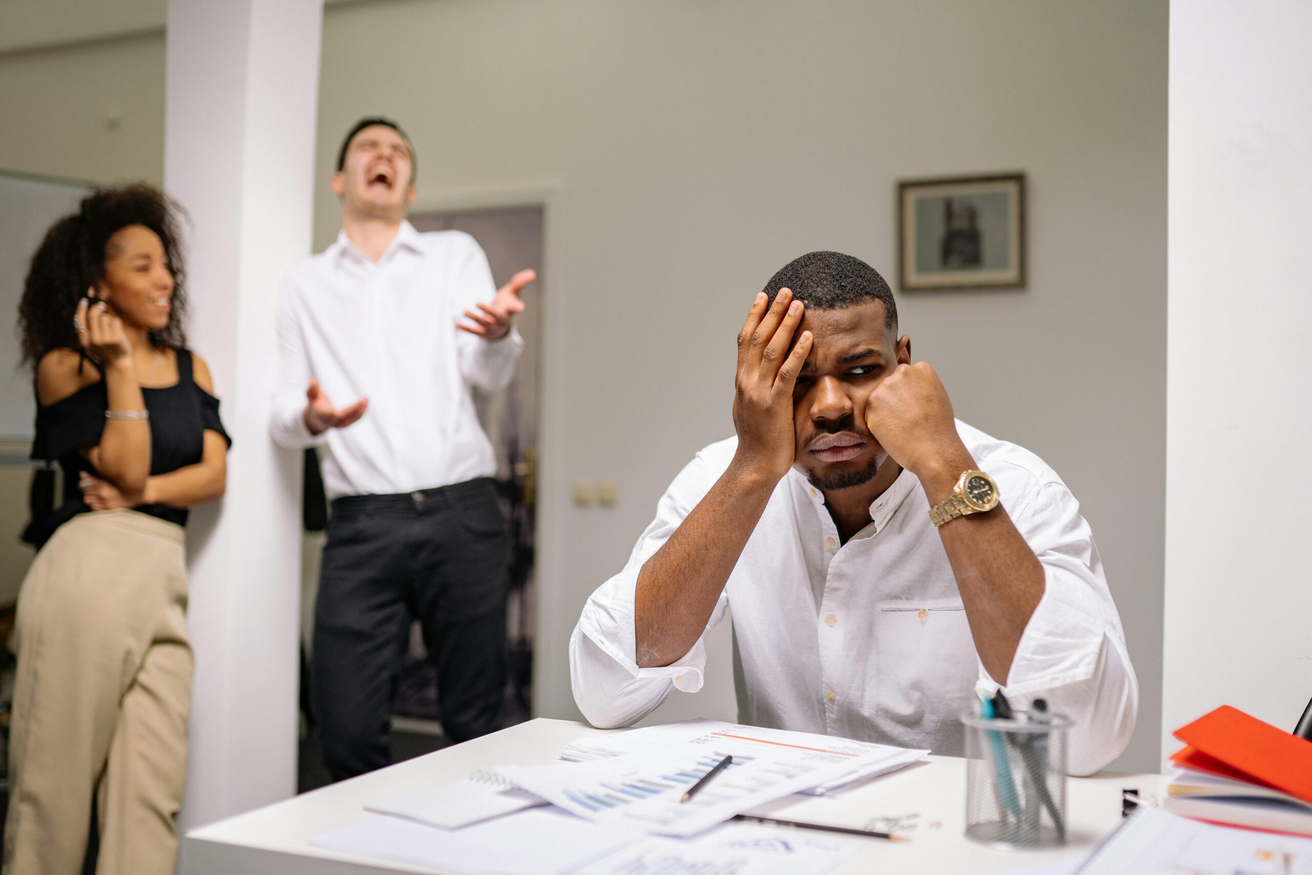 A man sitting alone at a desk while his coworkers socialize and enjoy themselves
